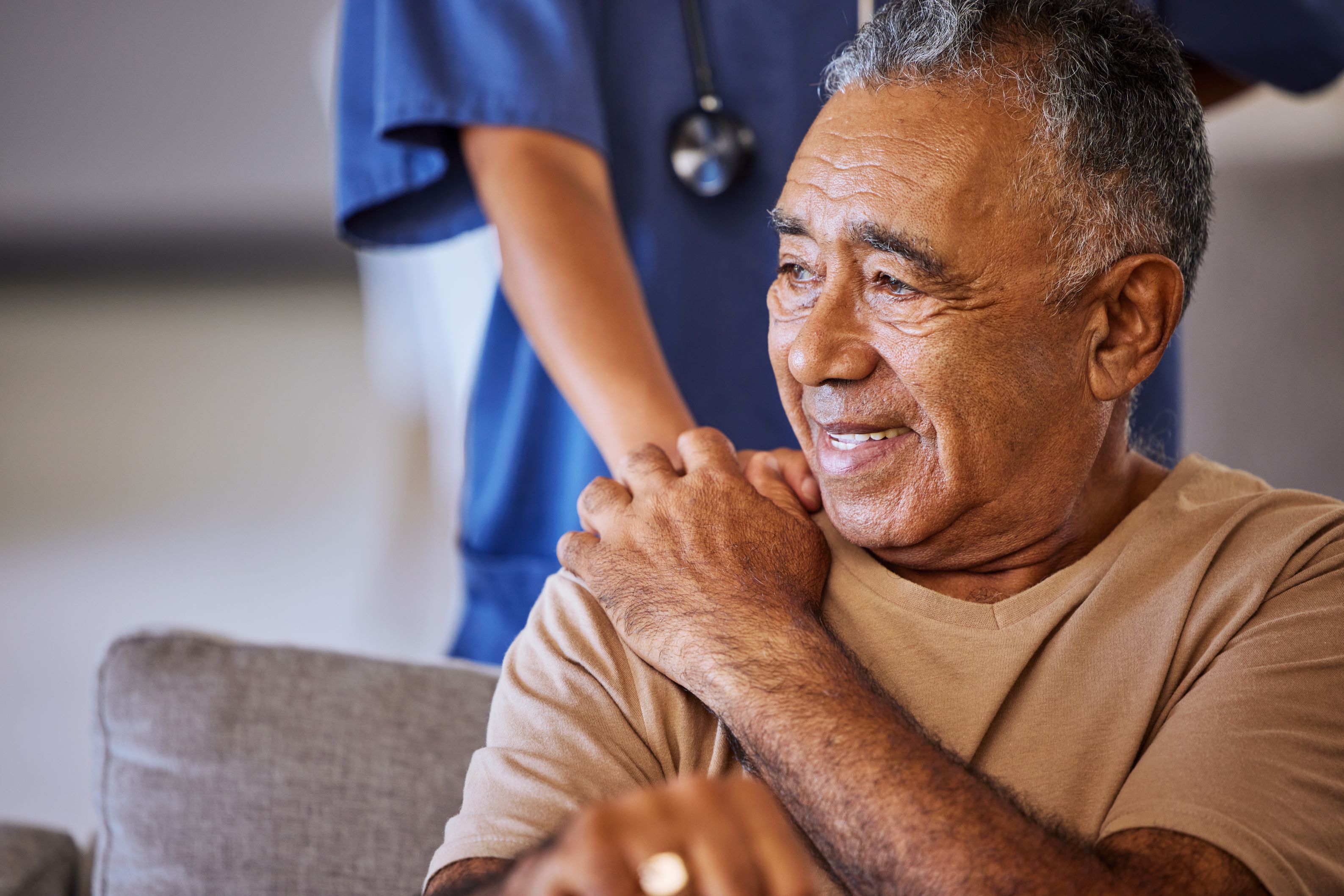 Senior Medicaid patient at home holds hand of home health care aide.